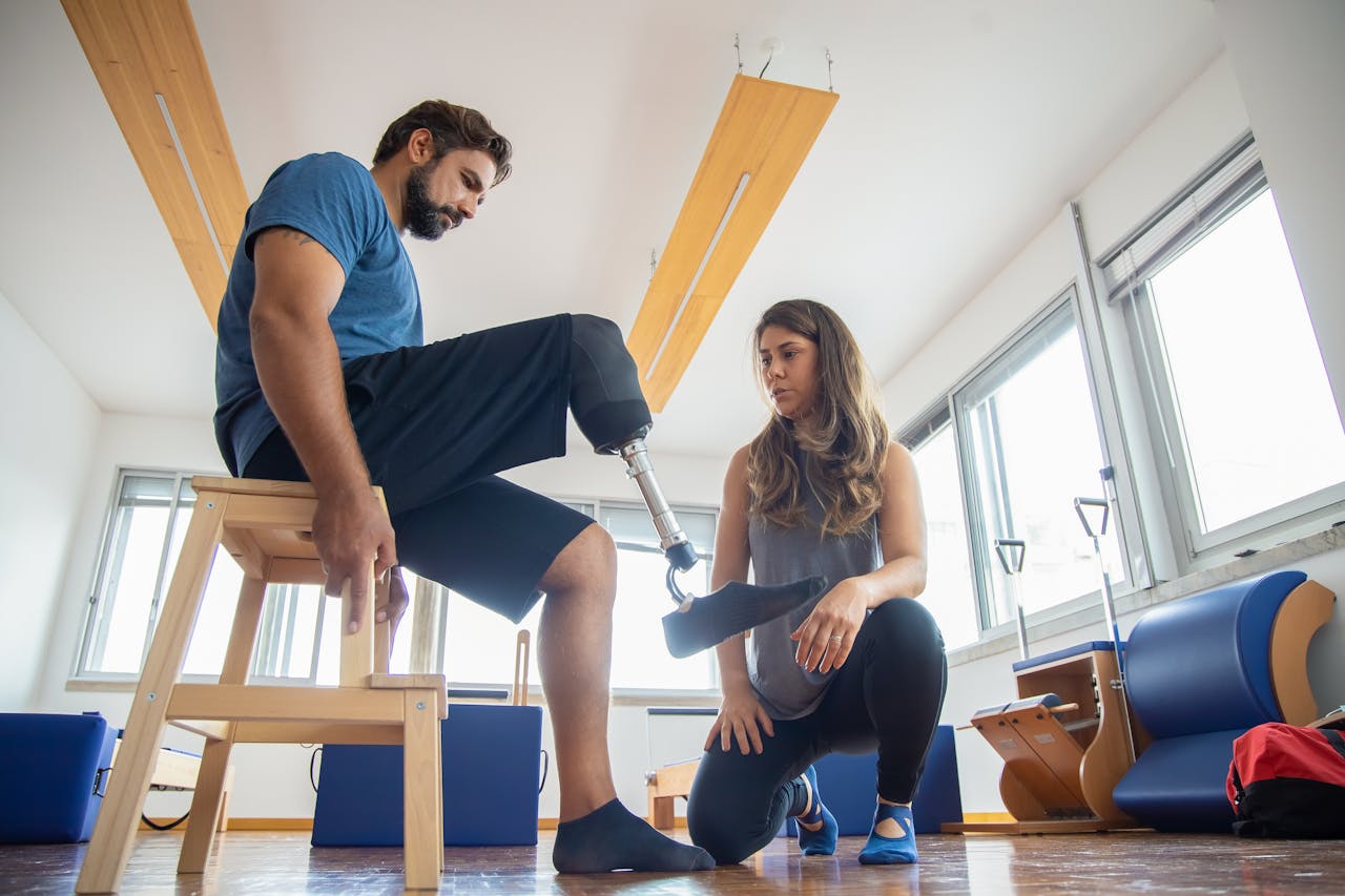 About A man with a prosthetic leg assisted by a therapist during rehabilitation indoors.